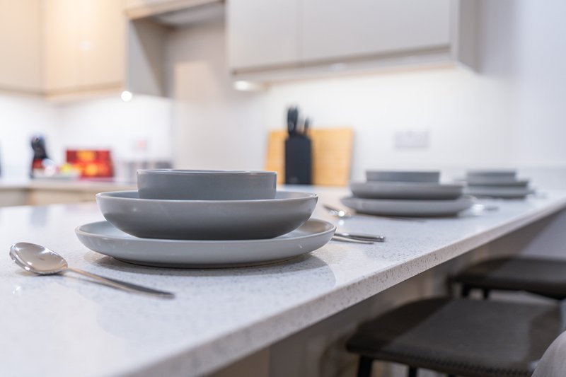 Modern kitchen with stacked plates, cutlery, and white countertop in focus
