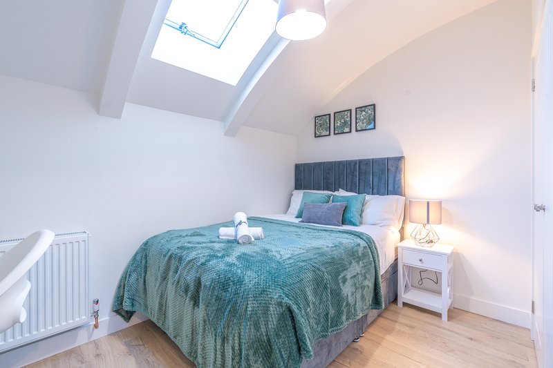 Bright attic bedroom with double bed, teal bedding, skylight window and wooden floor