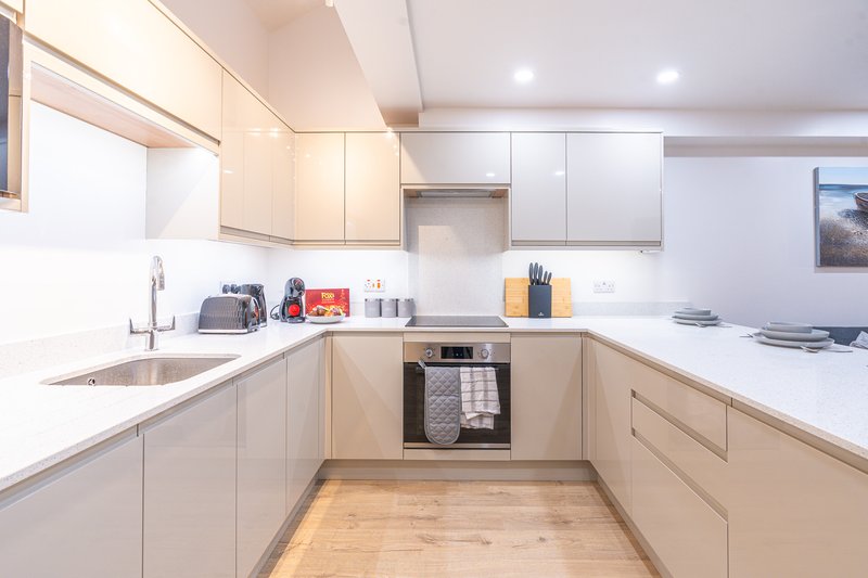 Modern kitchen with light wood cabinetry, white countertops, stainless steel oven and wooden flooring