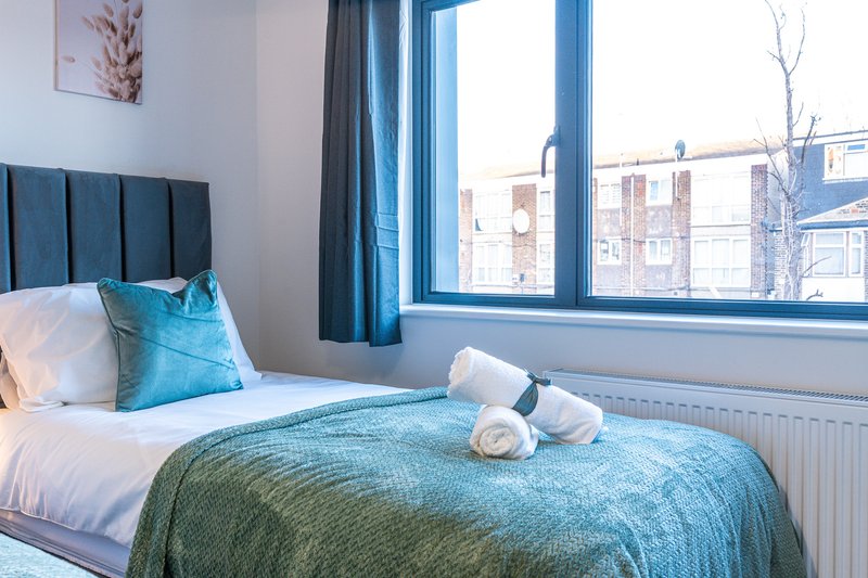 Modern bedroom with blue upholstered headboard, white bedding, blue throw, and city views from large window
