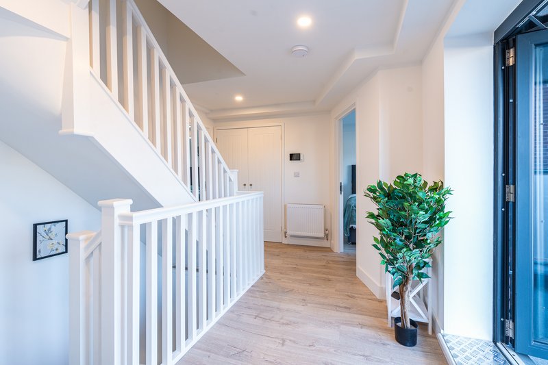 Modern hallway with white staircase, wooden flooring, potted plant and blue entrance door