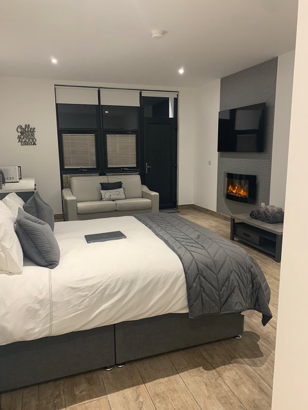 Modern bedroom with double bed, grey bedding, fireplace, seating area and large window