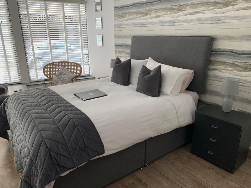 Modern bedroom with grey upholstered bed, white linens, decorative pillows and wooden accent wall