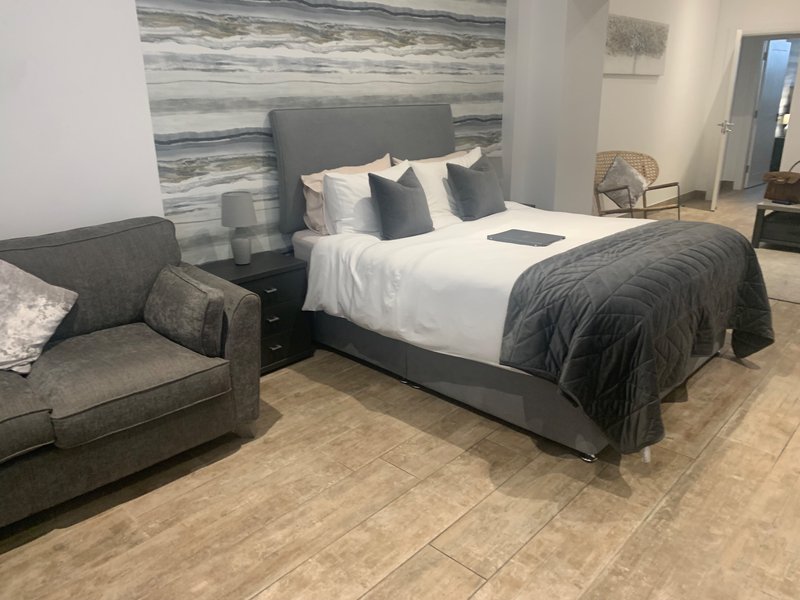 Modern bedroom with grey upholstered bed, white bedding, armchair, and wooden flooring