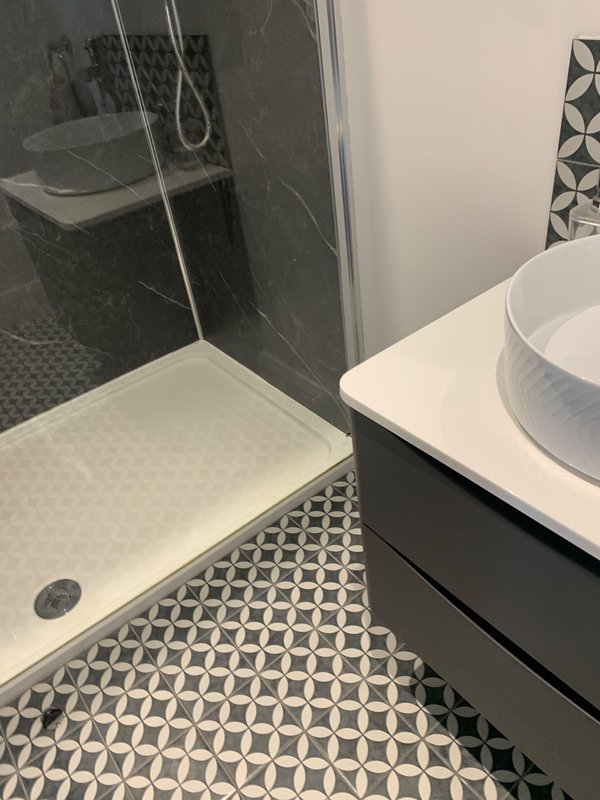 Modern bathroom with walk-in shower, geometric floor tiles, and white vanity sink