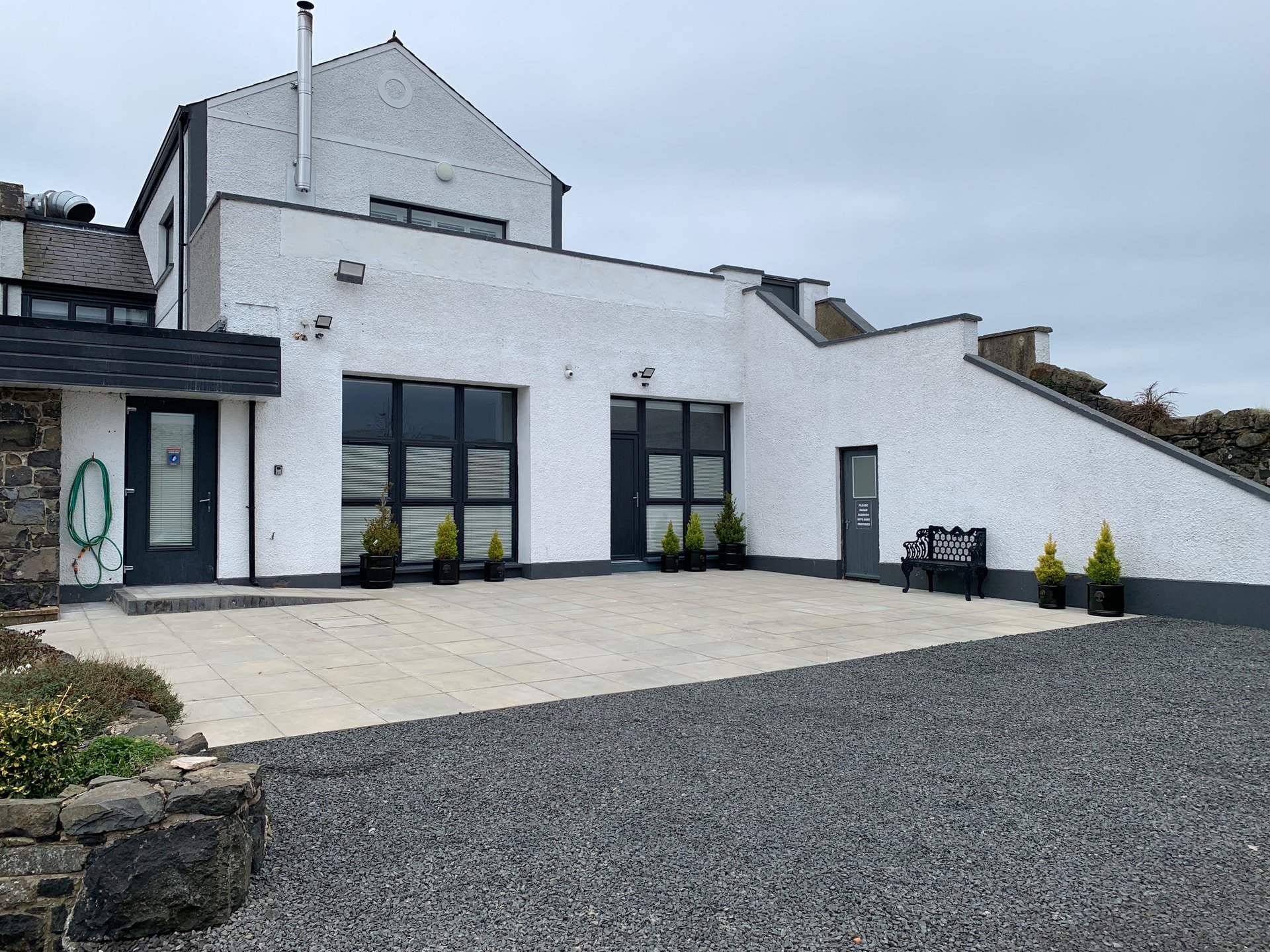 Modern white house exterior with driveway, paved terrace, and black-framed windows