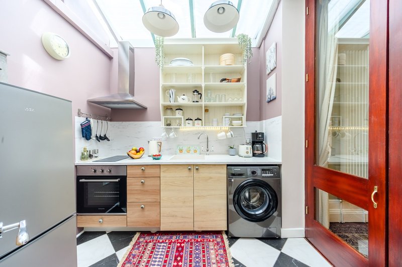 Modern kitchen with wooden cabinetry, black appliances, white countertop and colorful floor rug