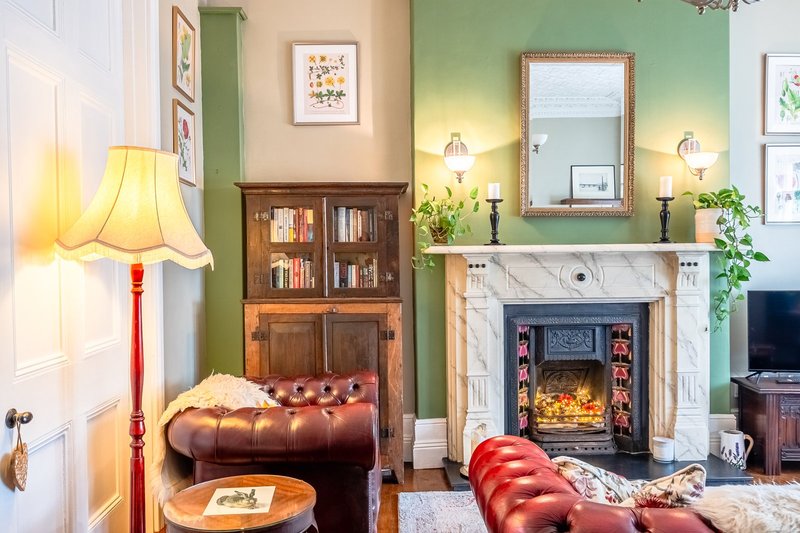 Living room with fireplace, leather seating, wooden bookcase, green accent wall and decorative artwork