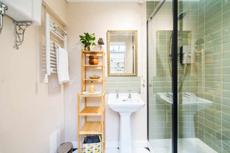 Bright bathroom with pedestal sink, glass shower enclosure, wooden shelving unit with towels and plants