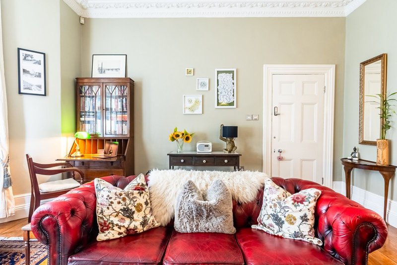 Living room with red leather sofa, decorative cushions, wooden furniture and framed wall art