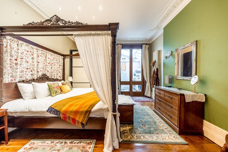 Bedroom with four-poster bed, green accent wall, wooden dresser and glass doors to balcony