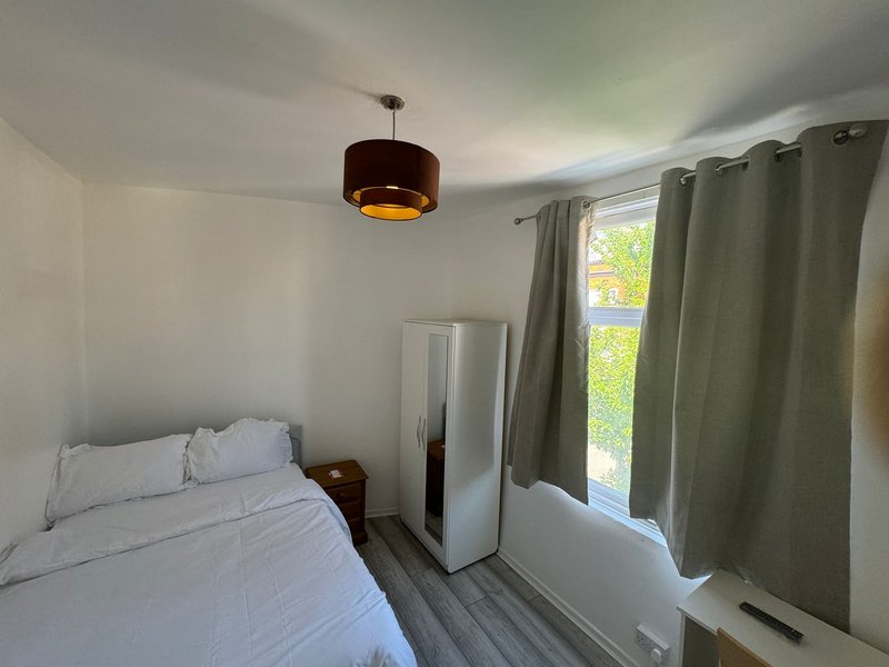 Bright bedroom with white bed, pendant light, wardrobe, and green curtains by window