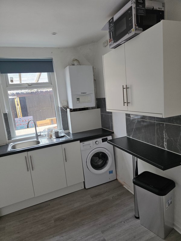 Modern kitchen with white cabinets, washing machine, microwave, and window overlooking garden