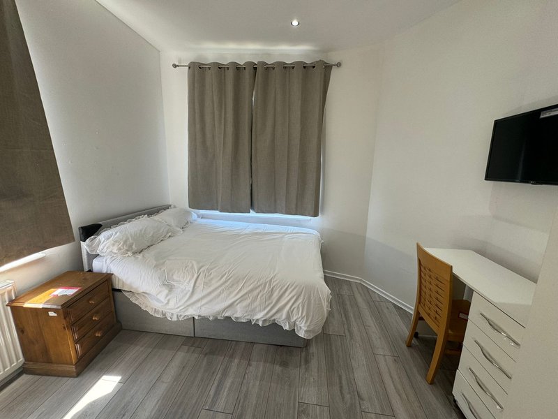Bright bedroom with double bed, wooden nightstand, wall-mounted TV and grey curtains