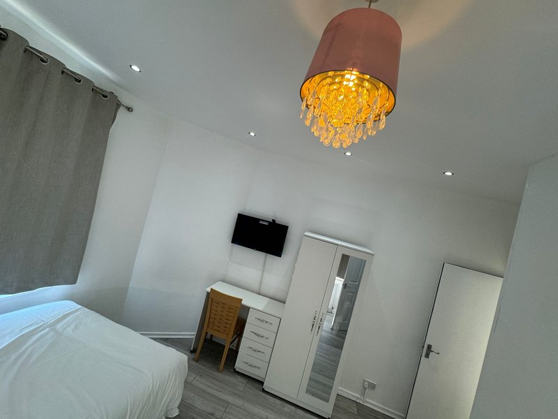 Modern bedroom with white bed, pendant light fixture, wall-mounted TV, and ensuite door