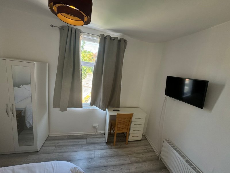 Bedroom with double bed, wall-mounted TV, wooden desk, curtained window and ceiling lamp