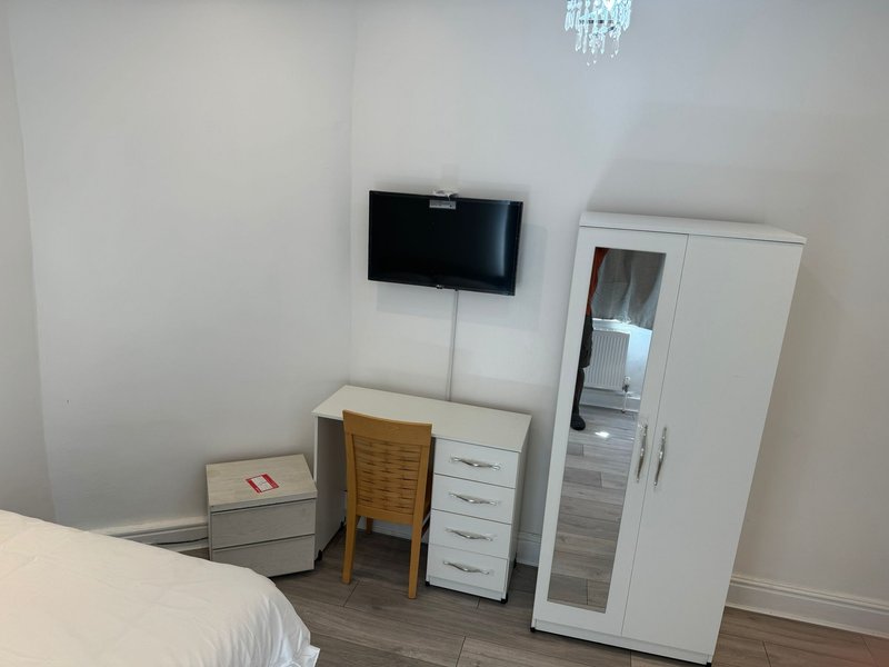 Bedroom with wall-mounted TV, desk, chair, white wardrobe and bedside furniture