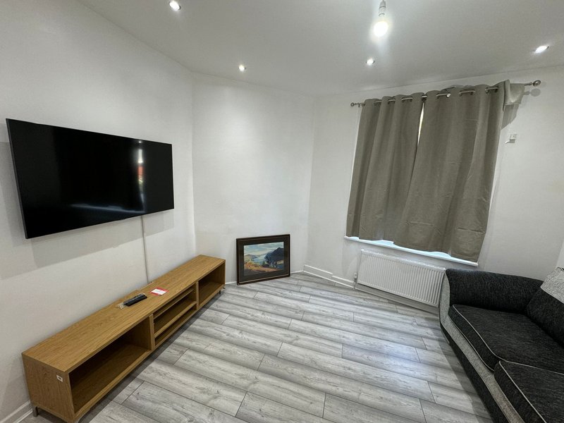 Modern living room with wall-mounted TV, wooden media console, striped flooring and black sofa