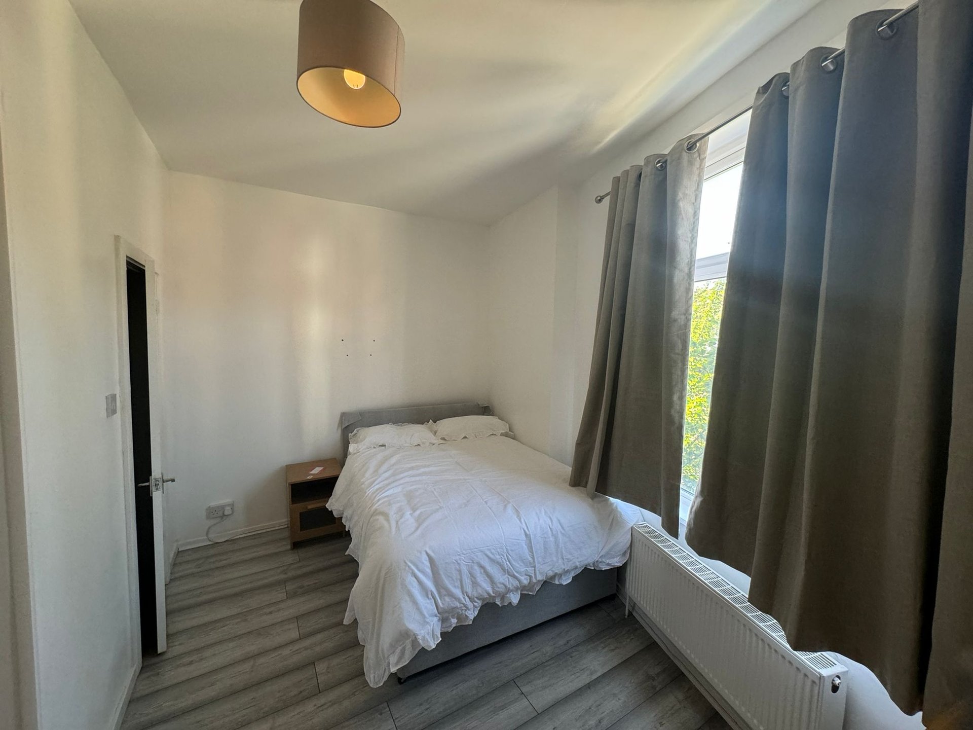 Bright bedroom with single bed, wooden flooring, pendant light and grey curtains