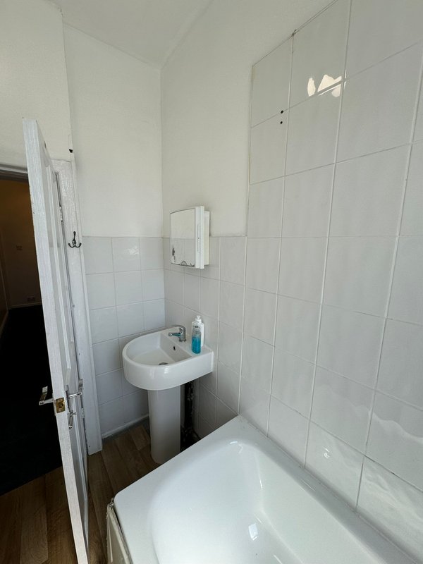 Small bathroom with white tiles, pedestal sink, bathtub and shower enclosure
