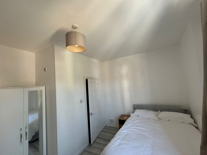 Bright bedroom with double bed, white wardrobe, ceiling lamp and sloped roof