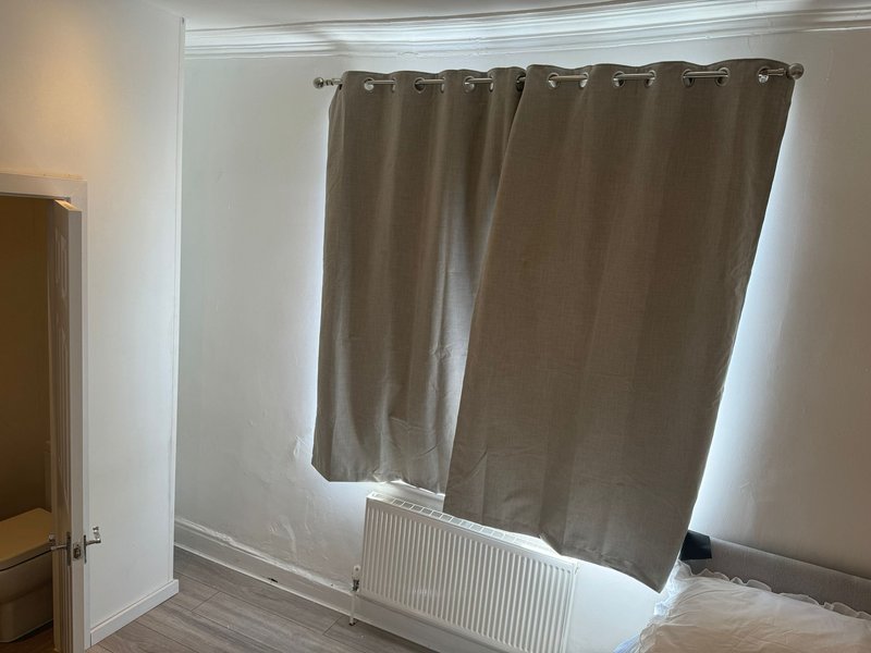 Bedroom with brown thermal curtains, radiator, wooden floor and white walls