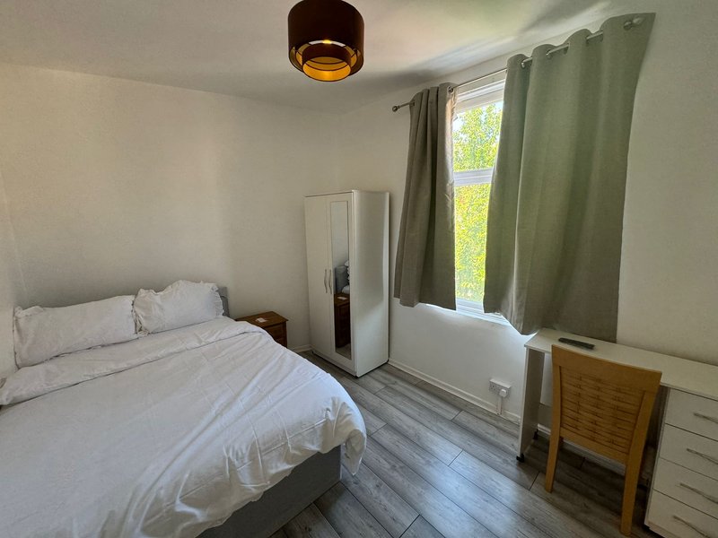 Bright bedroom with double bed, white bedding, green curtains, wooden chair and ceiling light