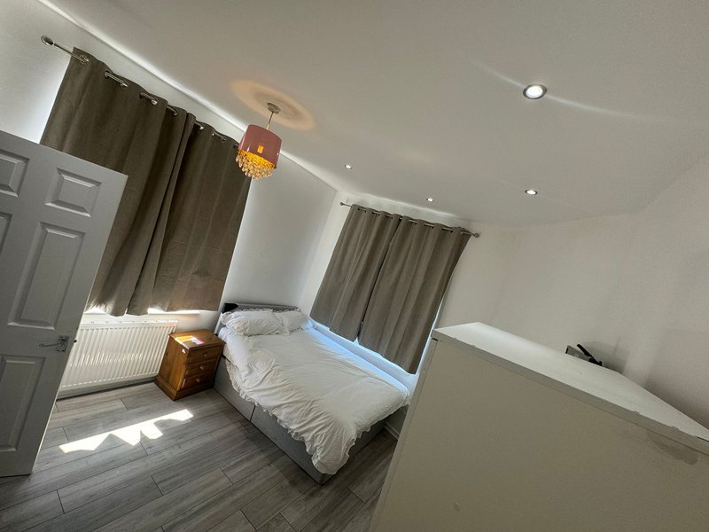 Bright bedroom with single bed, wooden floor, brown curtains and bedside table