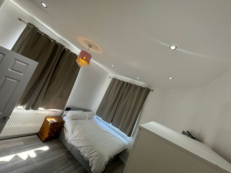 Bright bedroom with double bed, grey curtains, wooden floor and ceiling lights