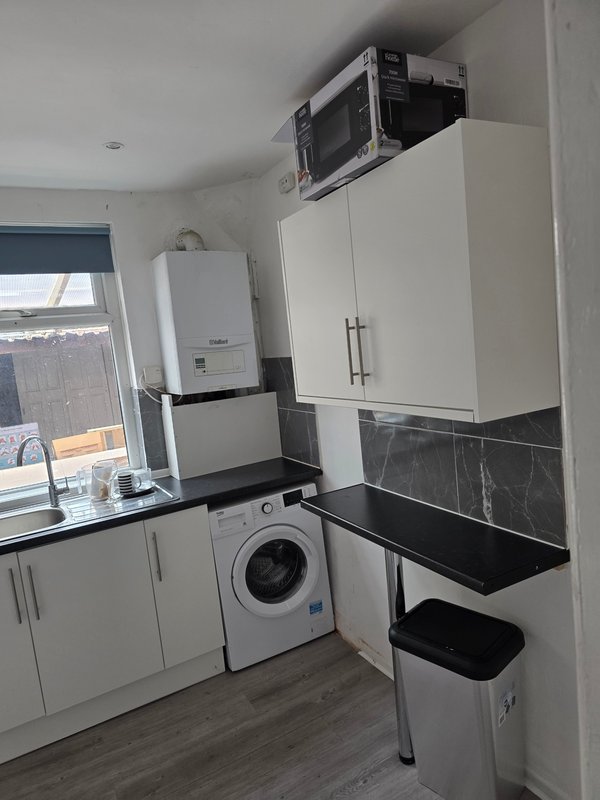 Modern kitchen with white cabinets, black countertop, washing machine and wall-mounted boiler