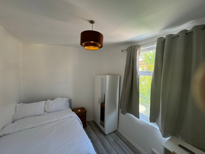 Bright bedroom with single bed, pendant light, wardrobe and window with green curtains