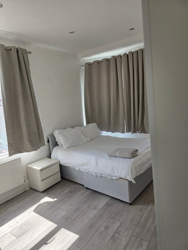 Bright bedroom with double bed, beige curtains, white pillows and grey wood flooring