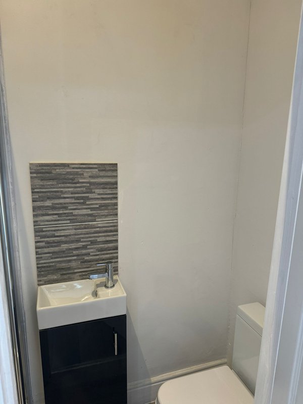 Compact bathroom with vanity sink, dark cabinet, striped tile backsplash and toilet