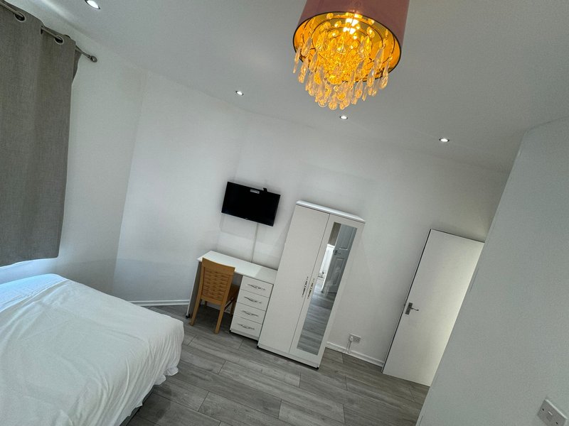 Modern bedroom with white bed, wall-mounted TV, yellow pendant light, and wooden flooring