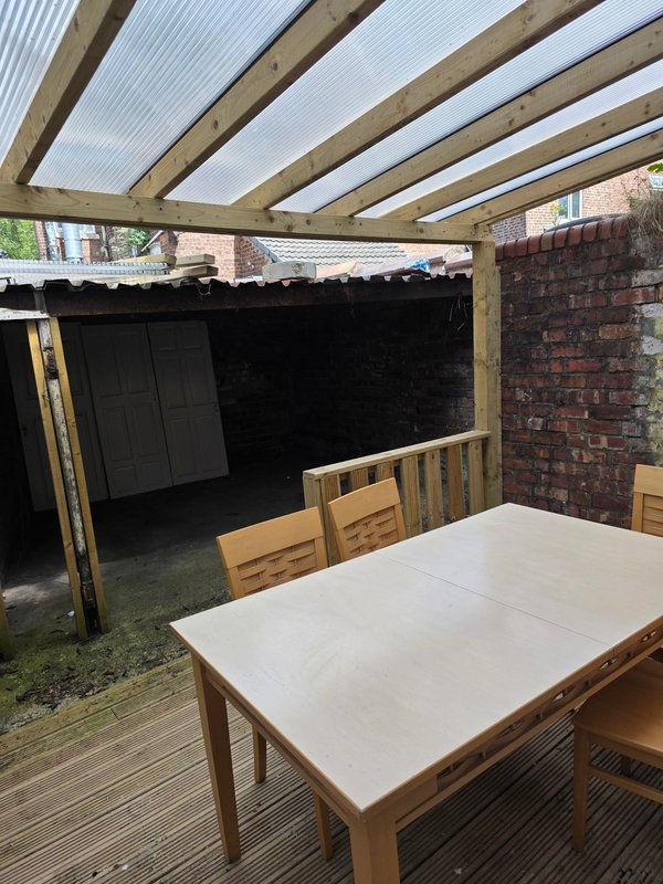 Covered patio area with wooden dining table, chairs, and brick outbuilding