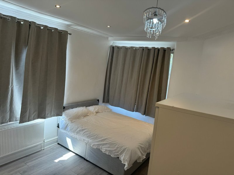 Bright bedroom with double bed, cream bedding, grey curtains, crystal chandelier and recessed lighting