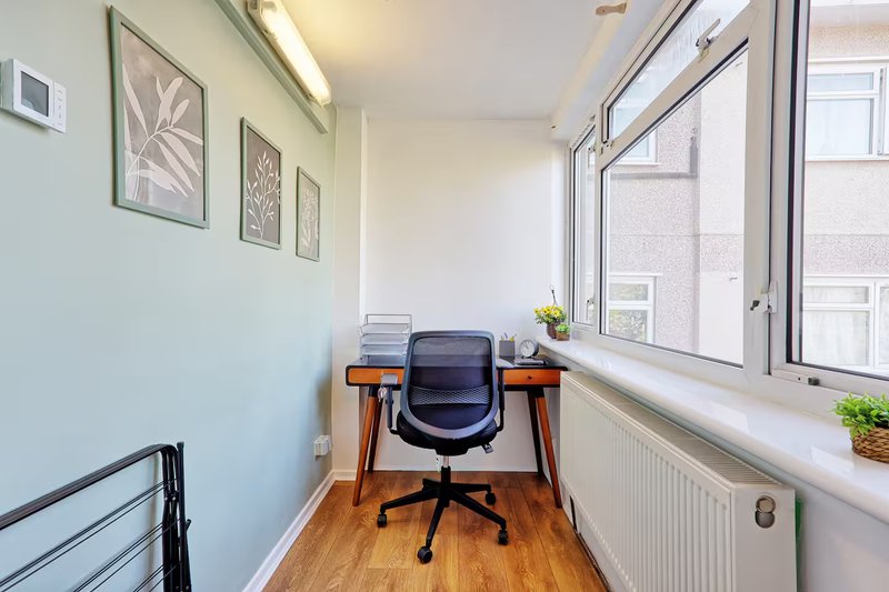 Bright home office with desk, black chair, wooden floor and large windows overlooking street