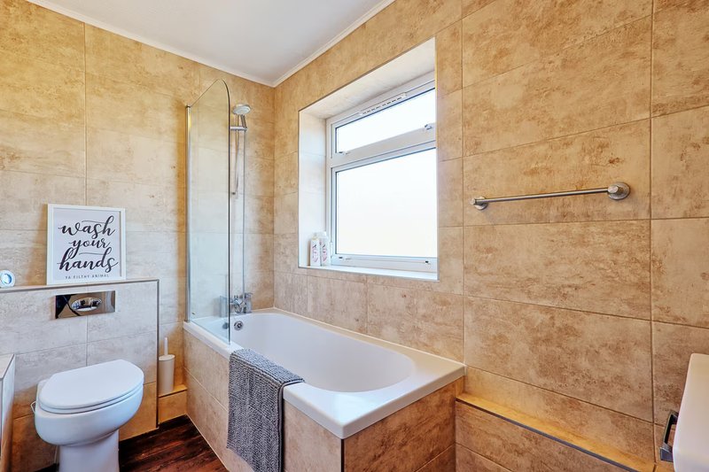 Modern bathroom with toilet, bathtub, shower enclosure, and beige tile walls