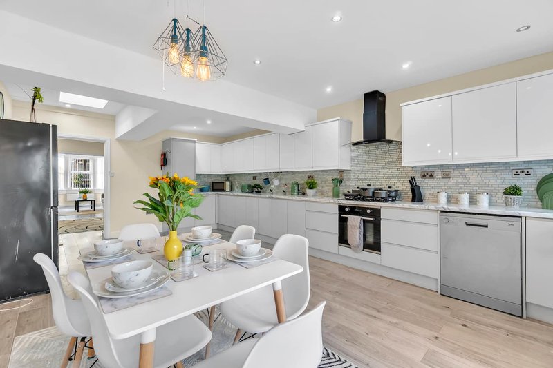 Modern open-plan kitchen and dining area with white cabinetry, stainless steel appliances, and dining table set for four