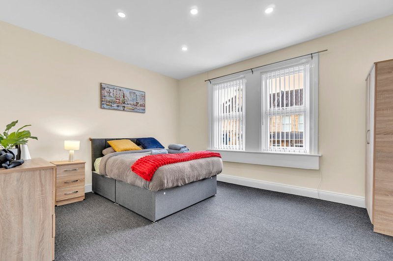 Bright modern bedroom with double bed, grey carpet, wooden furniture and vertical blinds on window