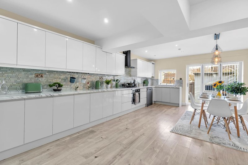 Modern open-plan kitchen and dining area with white cabinetry, green tile backsplash, and wooden flooring