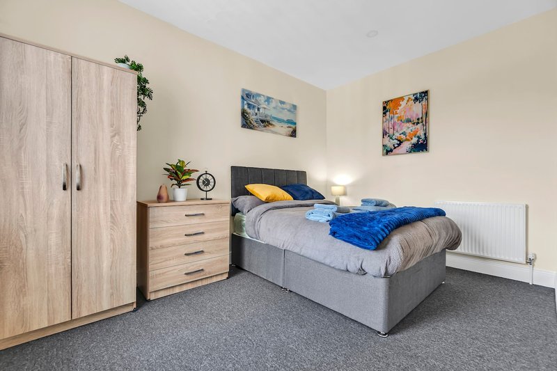 Bedroom with double bed, wooden wardrobe, chest of drawers, and wall art