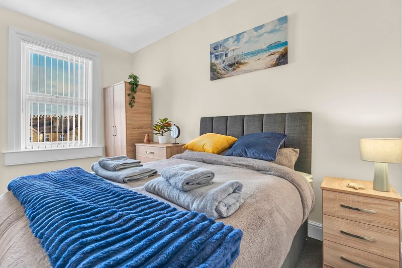 Bright bedroom with double bed, blue bedding, wooden furniture, and coastal wall art