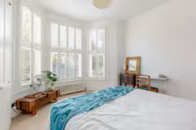 Bright bedroom with double bed, blue throw, wooden furniture and large windows