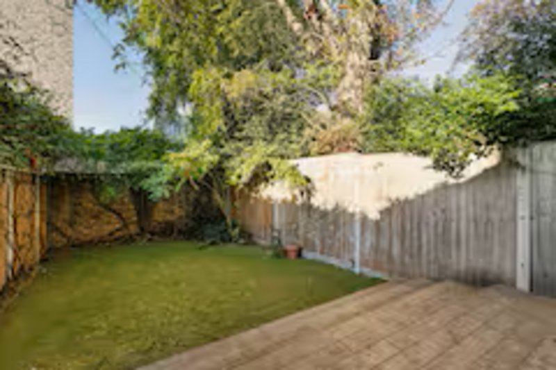 Spacious backyard with lawn, paved patio, wooden fencing and mature trees