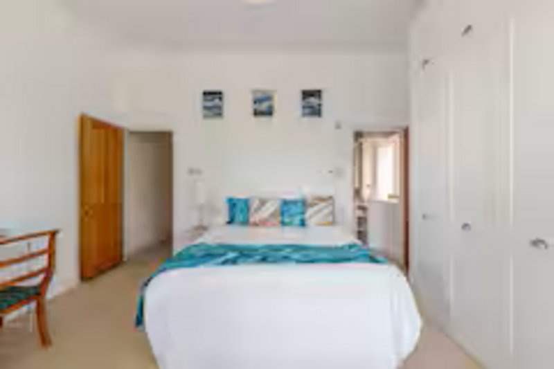 Bright bedroom with double bed, turquoise bedding, wooden door, and framed coastal artwork