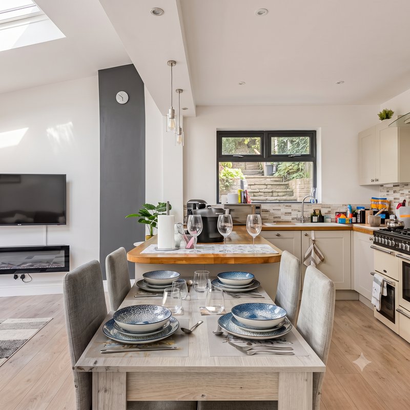 Modern kitchen and dining area with wood table, place settings, and cream cabinetry