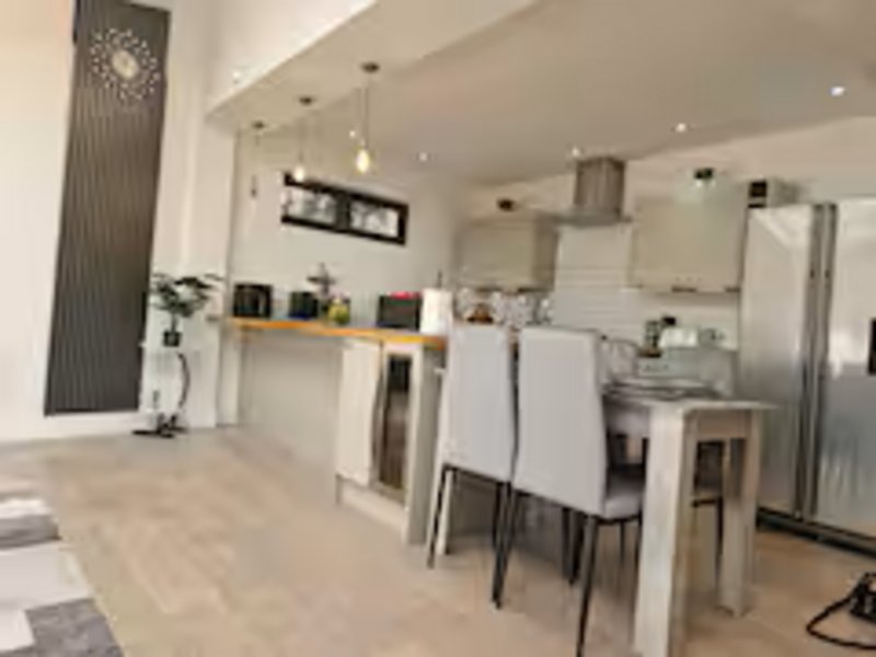 Modern open-plan kitchen and dining area with white cabinetry, stainless steel appliances, wooden shelving, and dining table with chairs