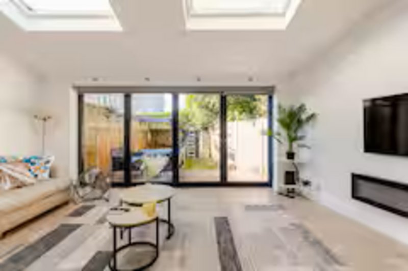 Bright modern living room with skylights, large glass doors opening to garden, sofa and TV