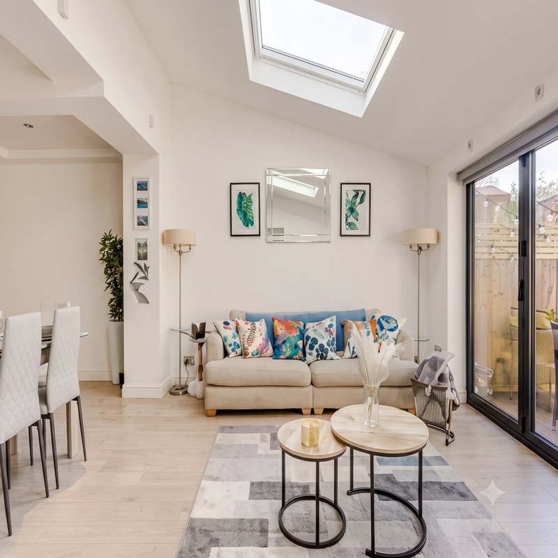 Bright modern living room with beige sofa, wooden coffee tables, skylights and glass patio doors